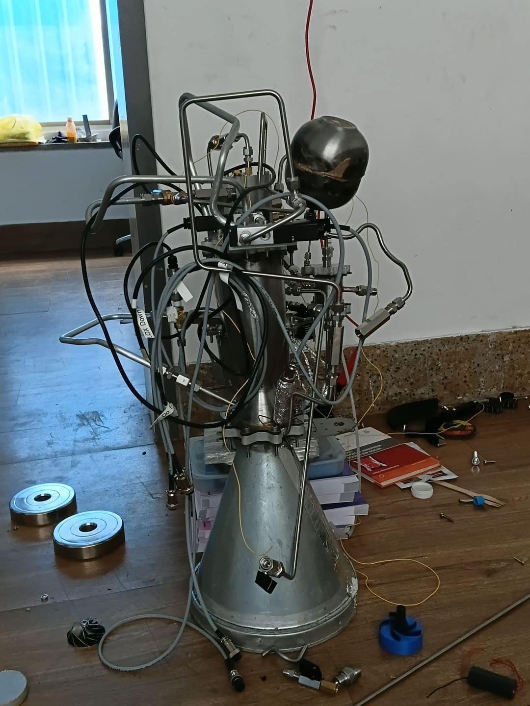 APEX propulsion development hardware standing on a workshop floor, with tubing, cabling and a spherical vessel above a large conical section.