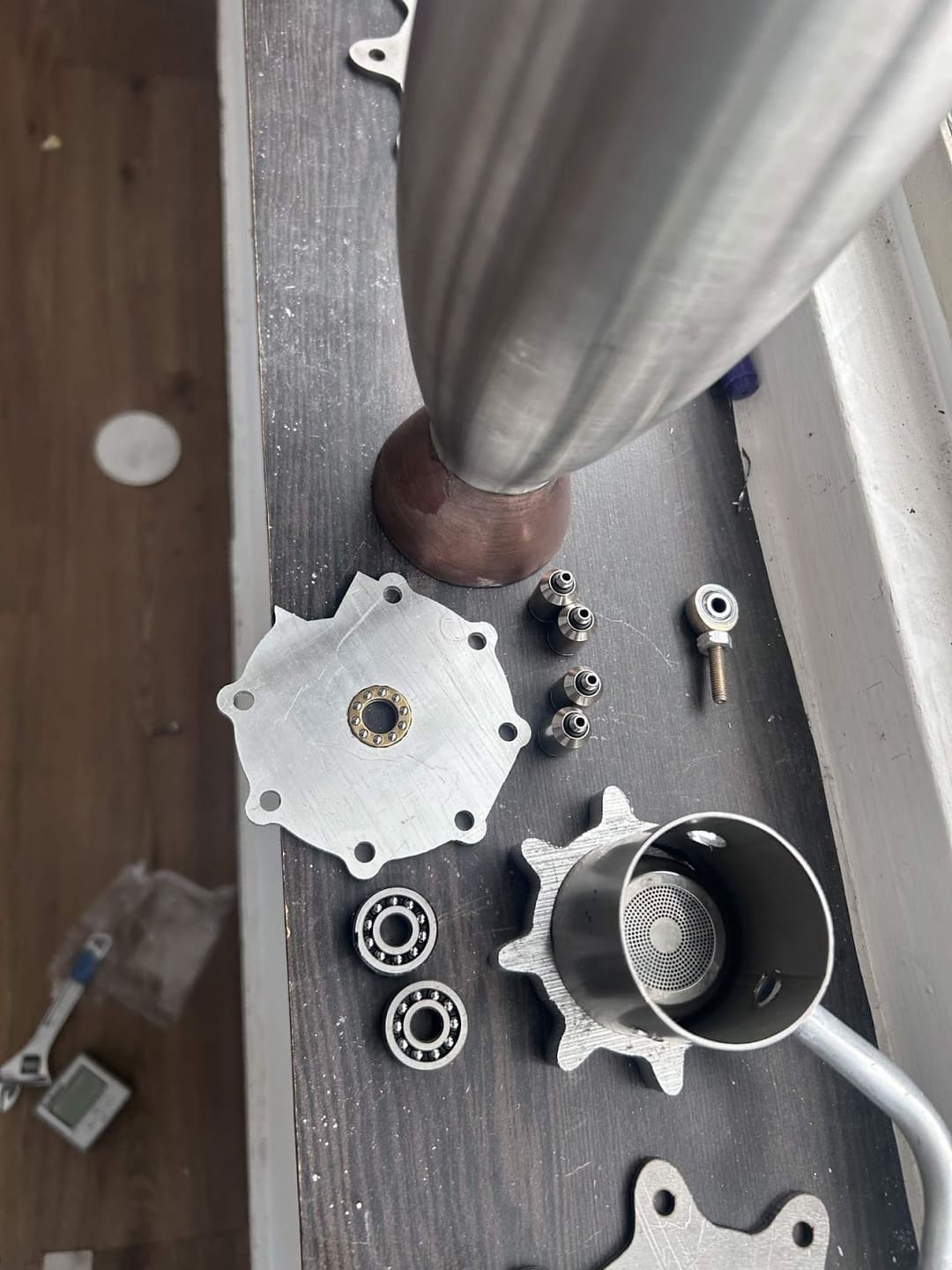 Machined and fabricated metal components laid out on a dark bench, including flanged plates, bearings and small fittings.
